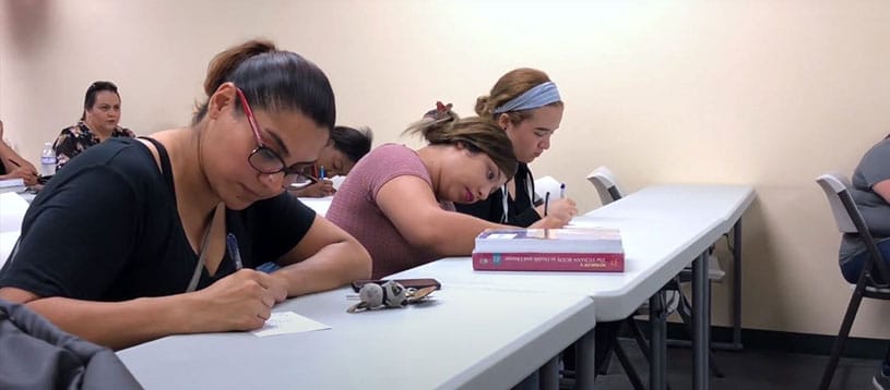 Students writing down high school equivalency notes in a classroom.